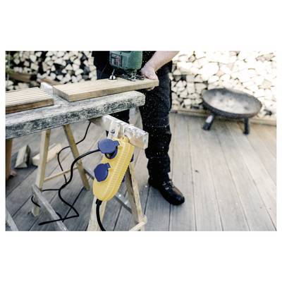 Person cutting a wooden plank with a circular saw on a workbench, using a yellow clamp or vise in a woodworking area.