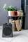 A small black fan heater stands on the floor in front of a side table with potted plants. Background: grey wall.