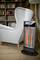 A grey armchair sits beside a switched-on electric heater in a living room with a bookshelf in the background.