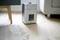A humidifier stands on a wooden floor next to a grey carpet and a sofa. The display shows 'StL'.