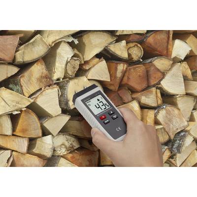 A hand holds a moisture metre against a stack of wood. The display shows 43% moisture.