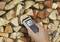 A hand holds a moisture metre against a stack of wood. The display shows 43% moisture.