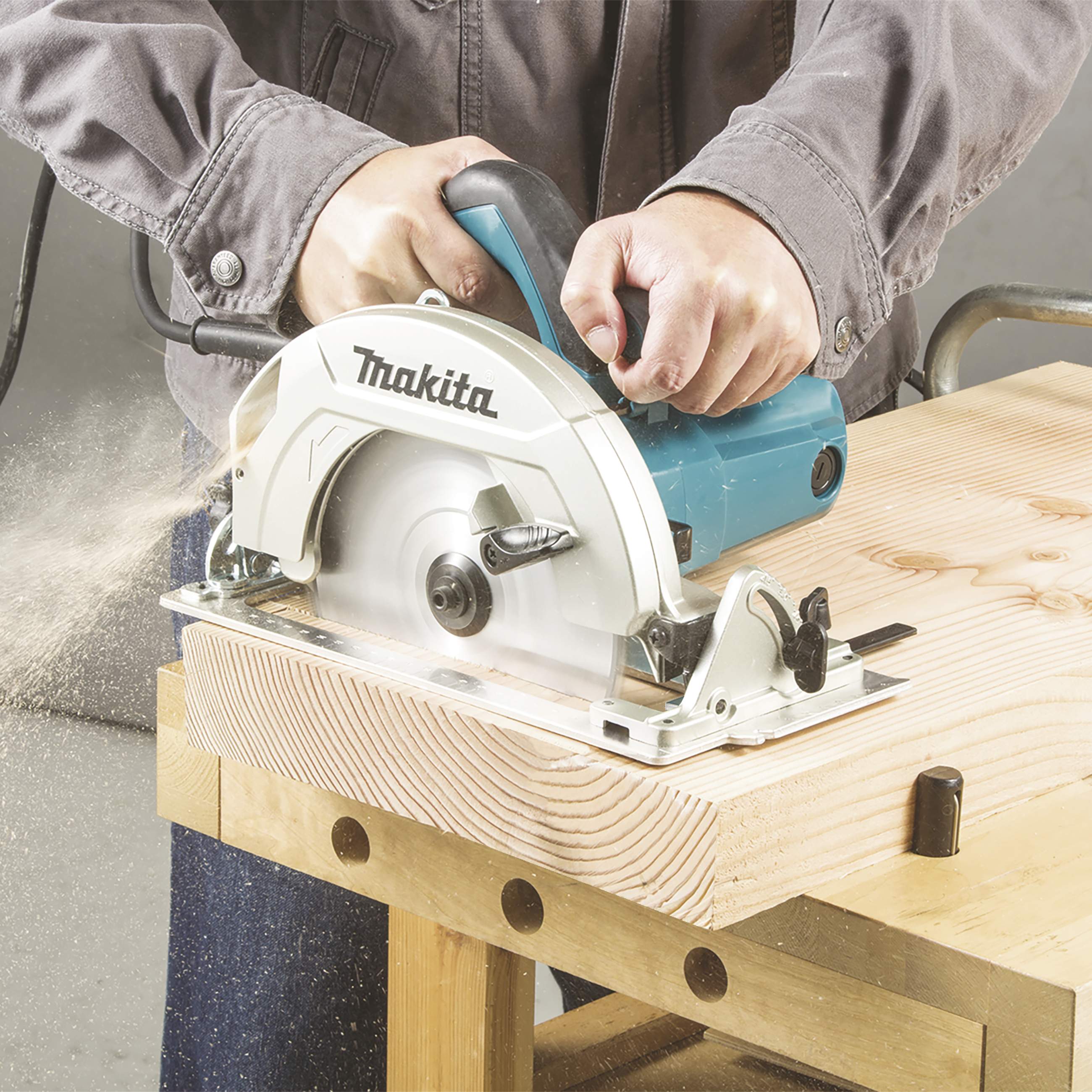 A person is sawing a wooden board with an electric circular saw. Wood shavings are flying off during the cutting process.