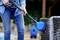 A person is cleaning a garden chair with a pressure washer. Water is spraying from the blue brush onto the chair.