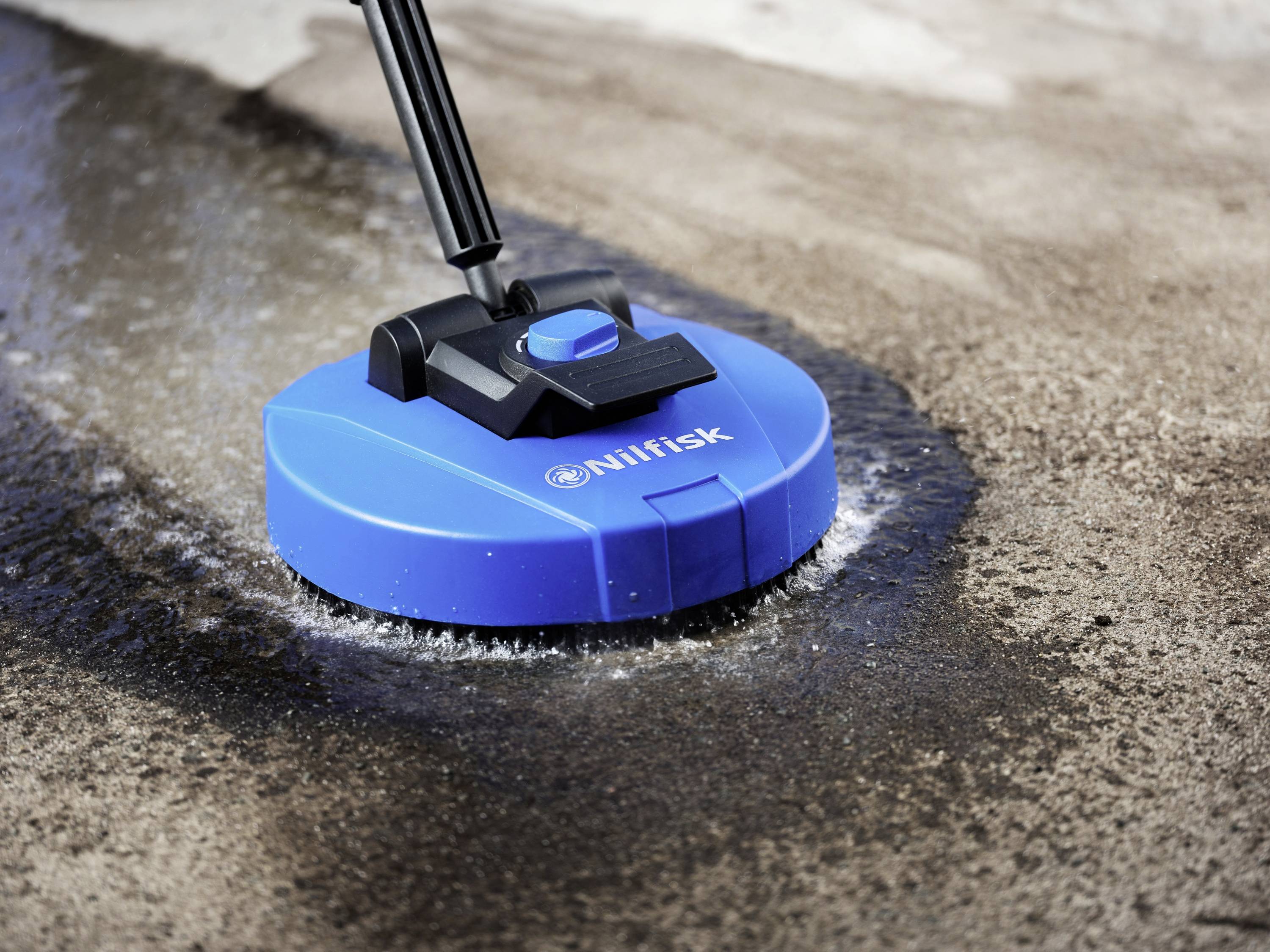 A blue floor cleaner with a handle is cleaning a concrete surface, with dirt and water visible.