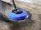 A blue floor cleaner with a handle is cleaning a concrete surface, with dirt and water visible.