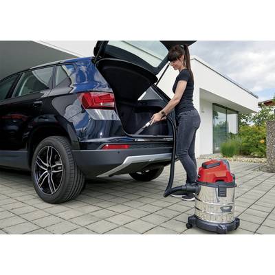 A woman is cleaning the boot of a black SUV with a vacuum cleaner. She is standing on a paved surface in front of a modern house.