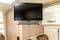 A flat-screen television with speakers is mounted on a wood-panelled wall, in the modern living area of a motorhome.