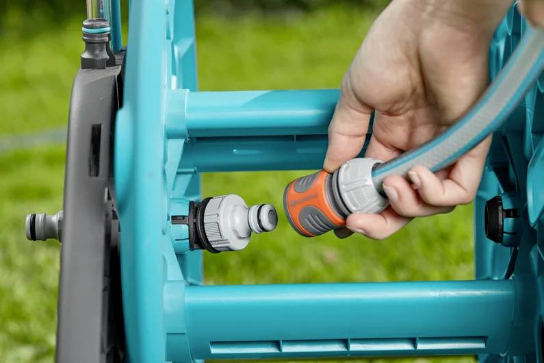 A hand connecting a garden hose to a hose reel on a lawn, illustrating hose setup.