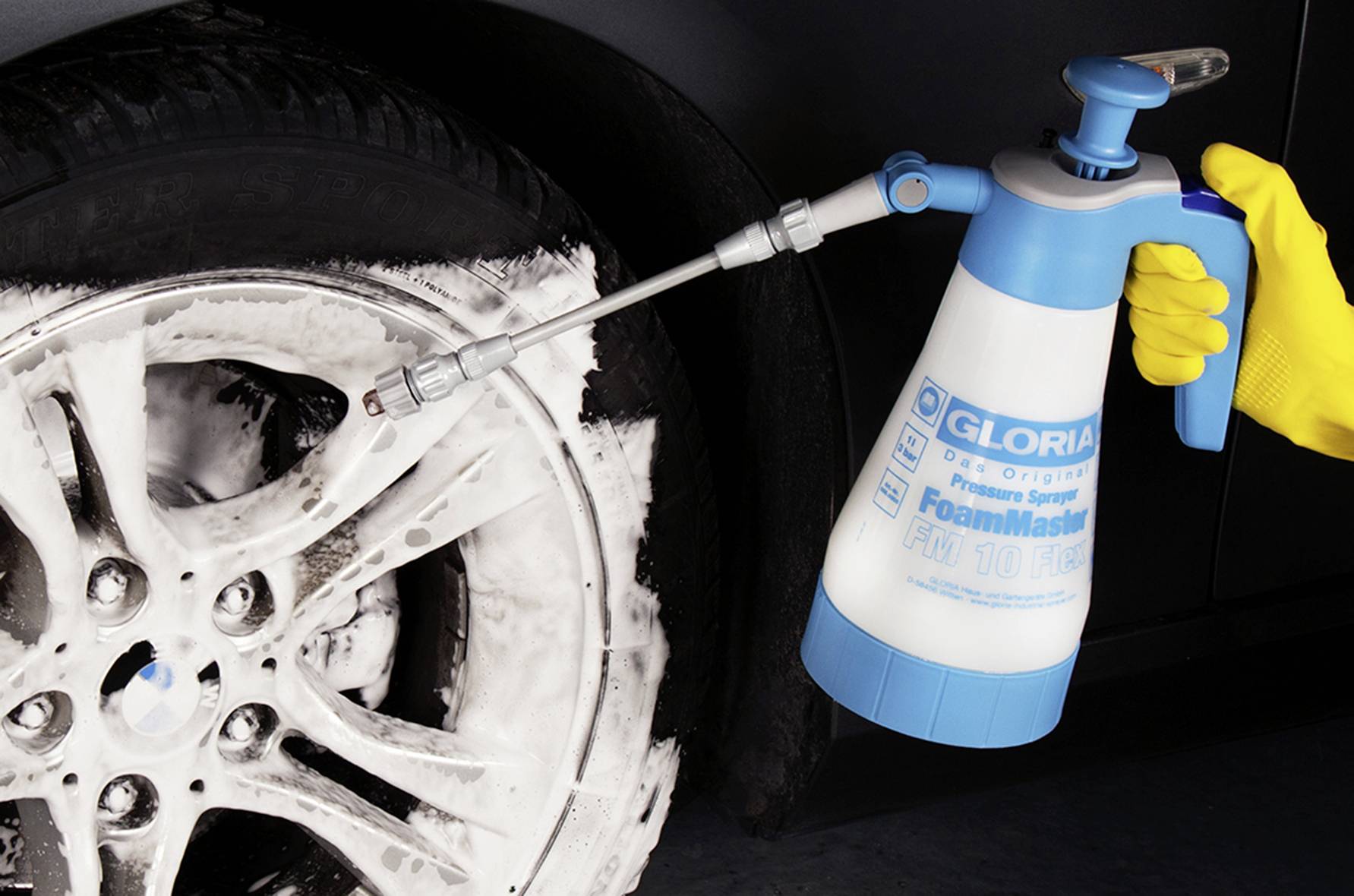 A person wearing yellow gloves is spraying foam onto a car tyre with a blue and white foam sprayer.
