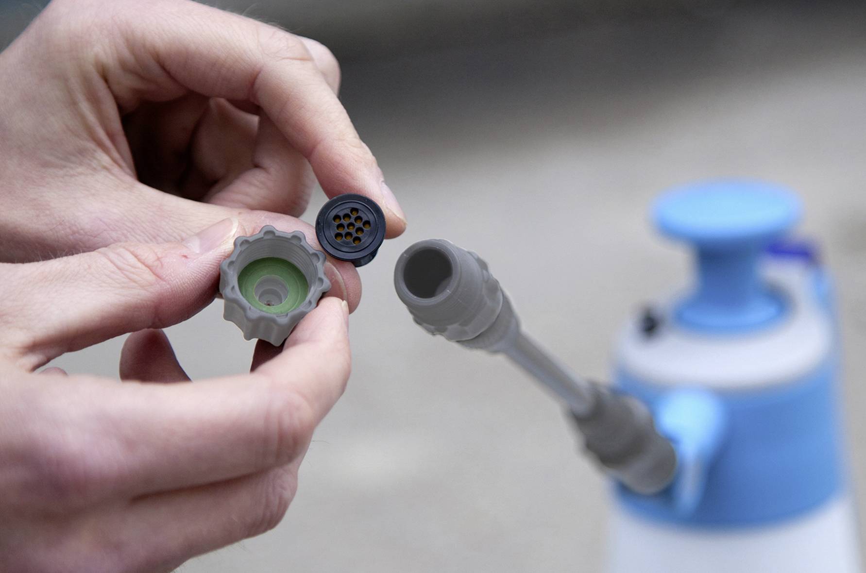 A person is holding a spray bottle nozzle and a removed filter, likely for cleaning or maintenance. The spray bottle is blurred in the background.