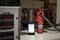 A digital multimeter is measuring the current in a workshop. A smartphone is displaying the same measurement. A machine is visible in the background.