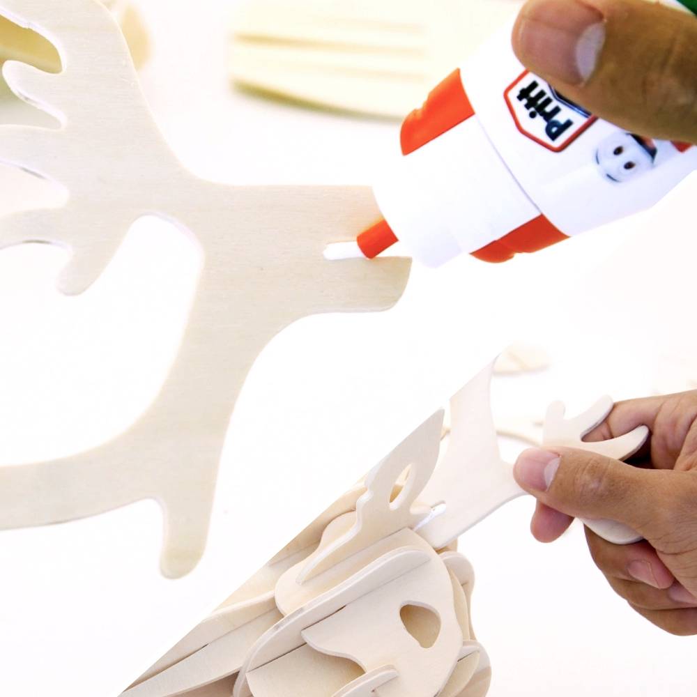 A person assembling wooden reindeer pieces with glue, focusing on hands holding a glue bottle and parts. Holiday decoration activity.
