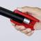 A hand is holding a red pepper spray with a black handle and spray mechanism. The trigger mechanism is visible.