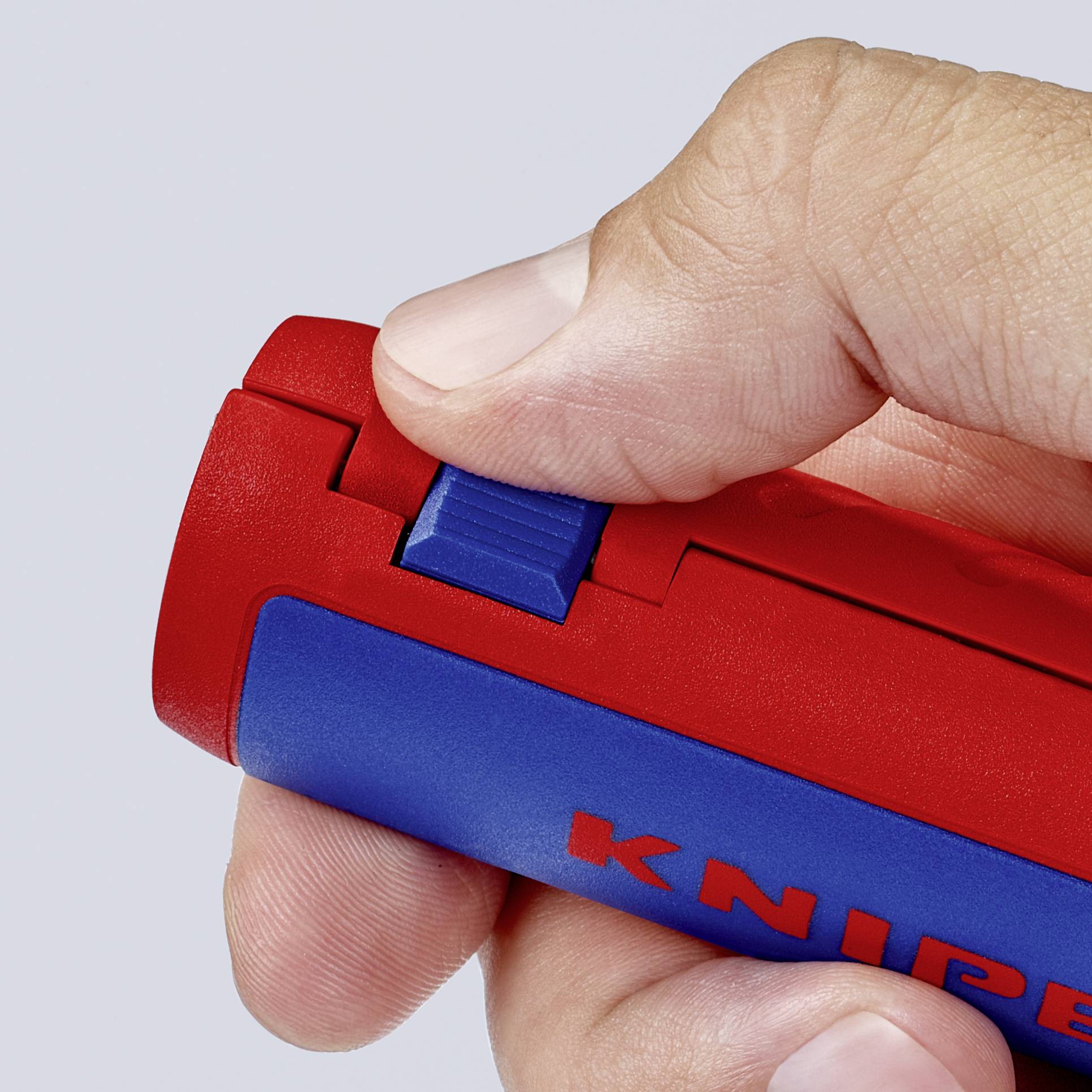 A hand operates the slider of a red utility knife, preparing it for use.