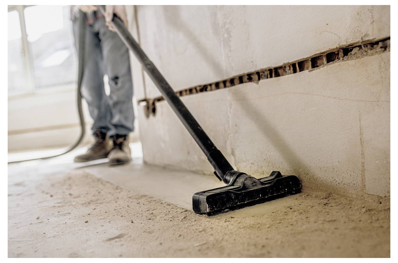 Person vacuuming debris in a partially renovated room, with exposed wall sections and construction dust visible.