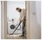 A person vacuums the floor in a laundry room with a washing machine and cleaning supplies visible in the background.