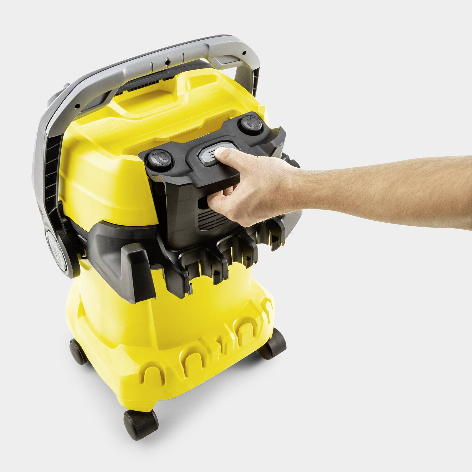 A person demonstrates removing a black part from a yellow and black vacuum cleaner on a white background.