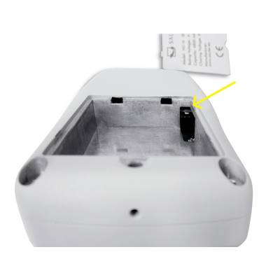 Underside of a white device with battery cover removed, revealing an open battery compartment. A yellow arrow points to a switch within the compartment.