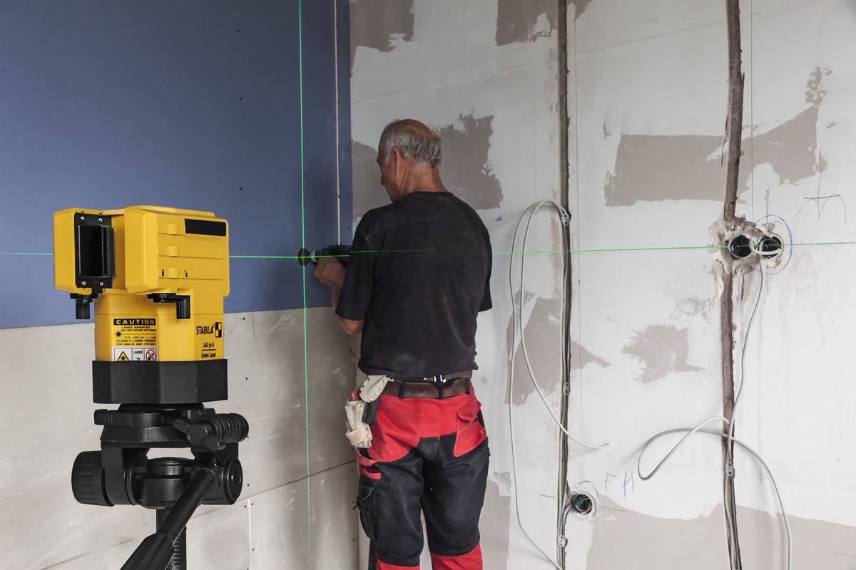 A person is working in a room with unfinished walls, using a yellow laser to project lines, possibly for construction work.
