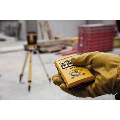 A gloved hand is holding a yellow control device, with a tripod blurred in the background.