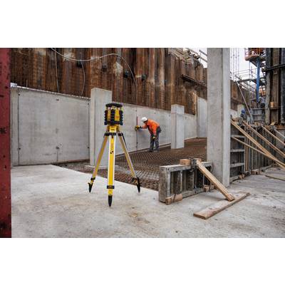 On a construction site, a worker in orange clothing is aligning the metal reinforcement. A surveying instrument is in the foreground.
