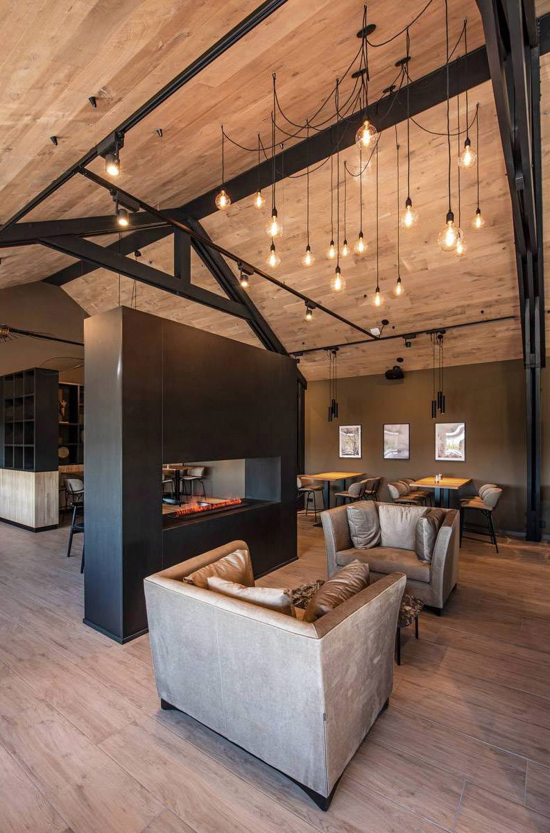 Modern room with a wooden ceiling, stylish lighting and comfortable armchairs. A fireplace separates the seating area from the rear dining area.