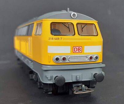Yellow and gray model train locomotive with DB logo, viewed from the front, on a black background.