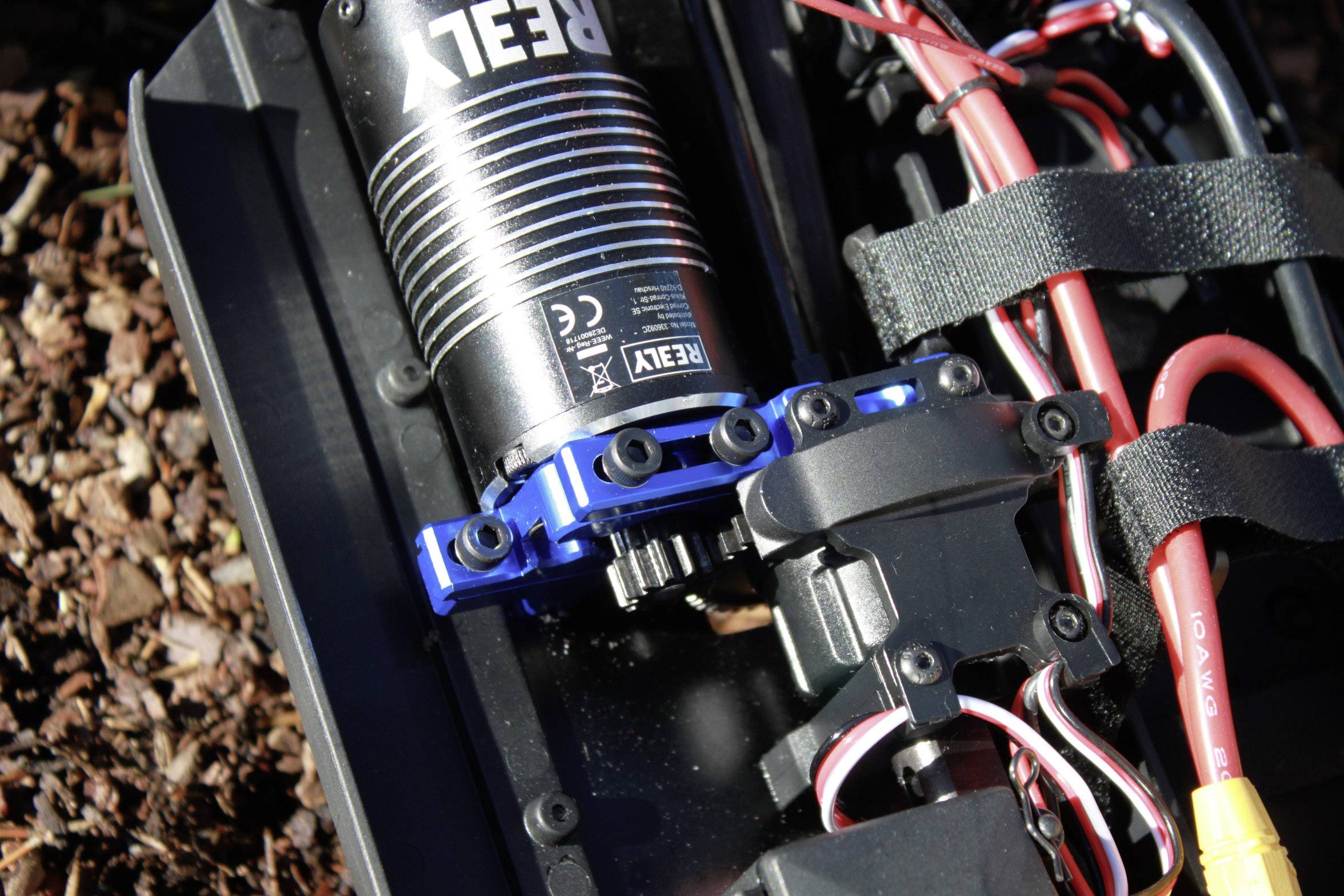 Electric motor of an RC car on a forest path, with cables and mounting brackets visible.