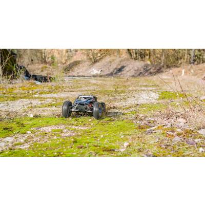 A remote-controlled car speeds along a moss-covered, rocky path in a natural setting with trees in the background.