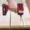 A person is tightening a screw into a wooden plank using a red cordless drill driver.