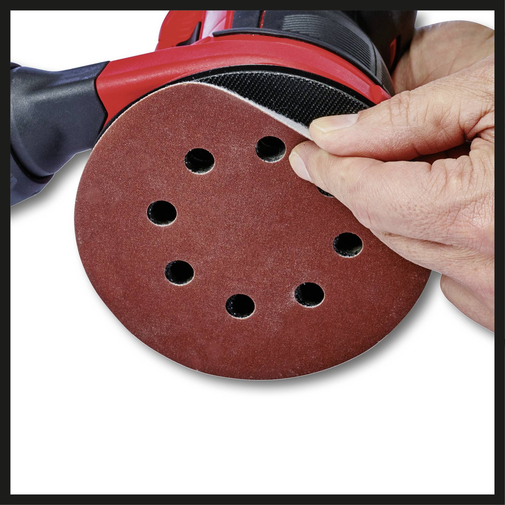 A hand changes the sandpaper on a round, red orbital sander with six holes.
