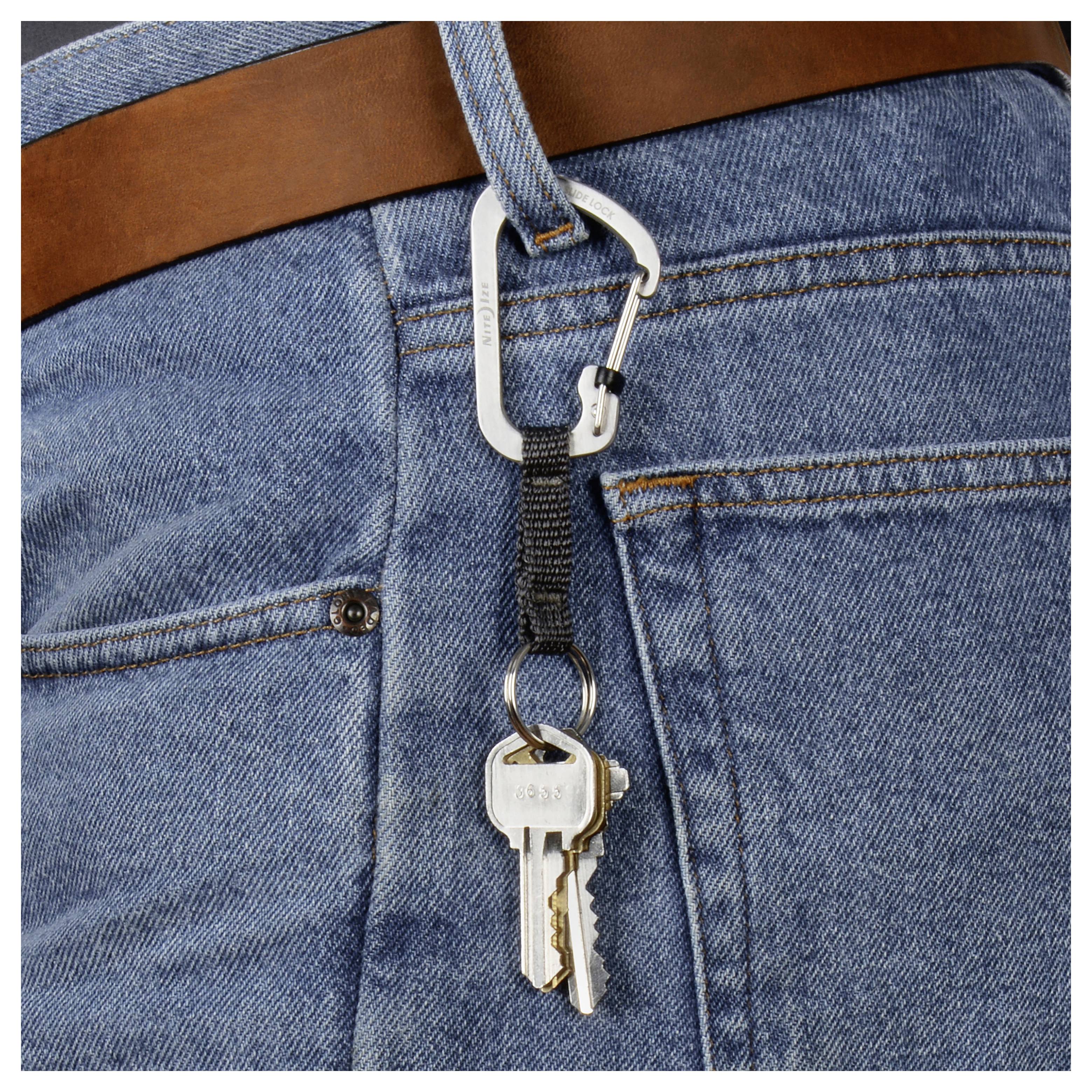 A carabiner attached to a belt loop of blue jeans holds two metal keys.