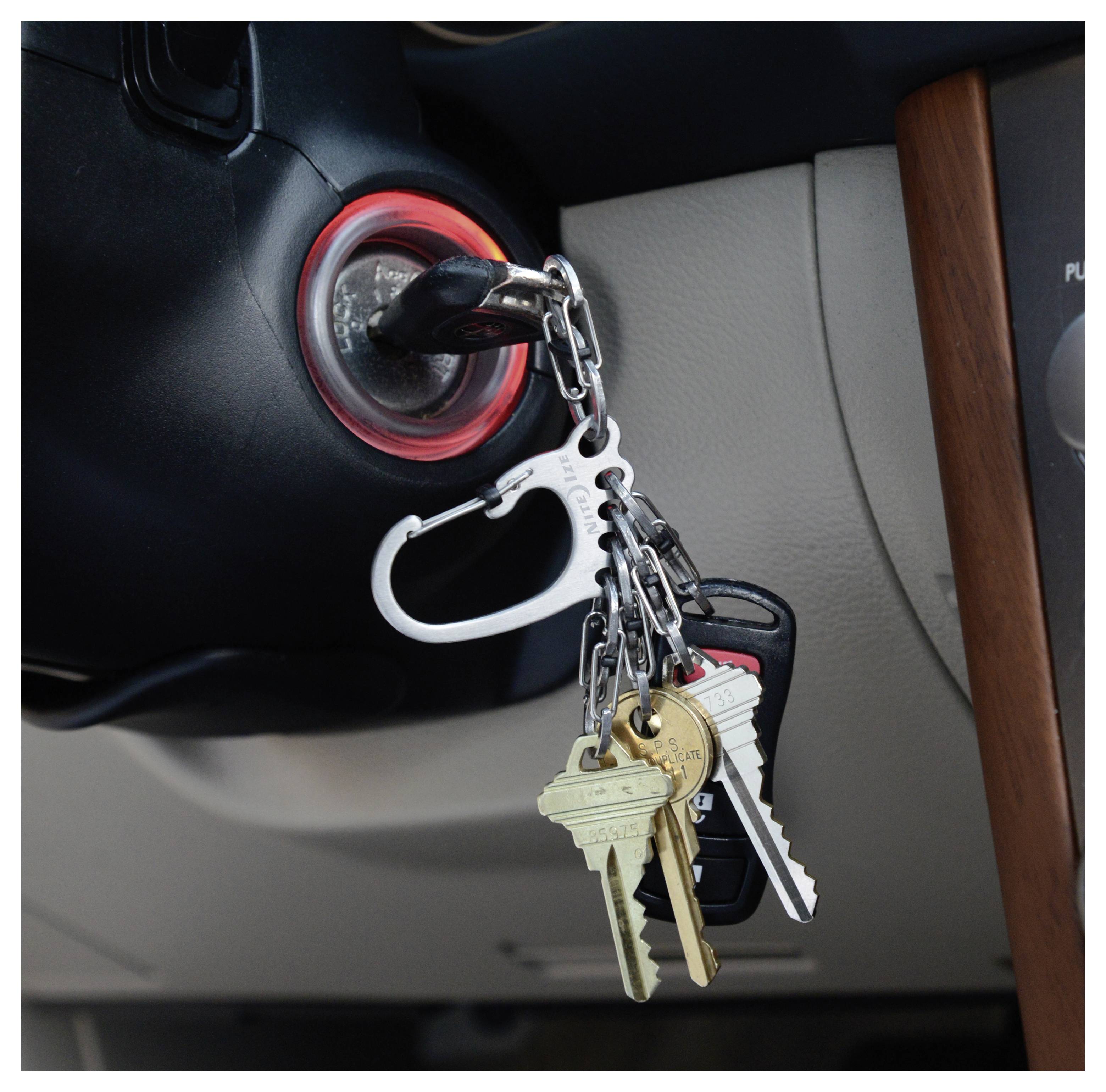 Car ignition with keys inserted, including a car key, house keys, and a carabiner keychain, in the ignition of a vehicle.