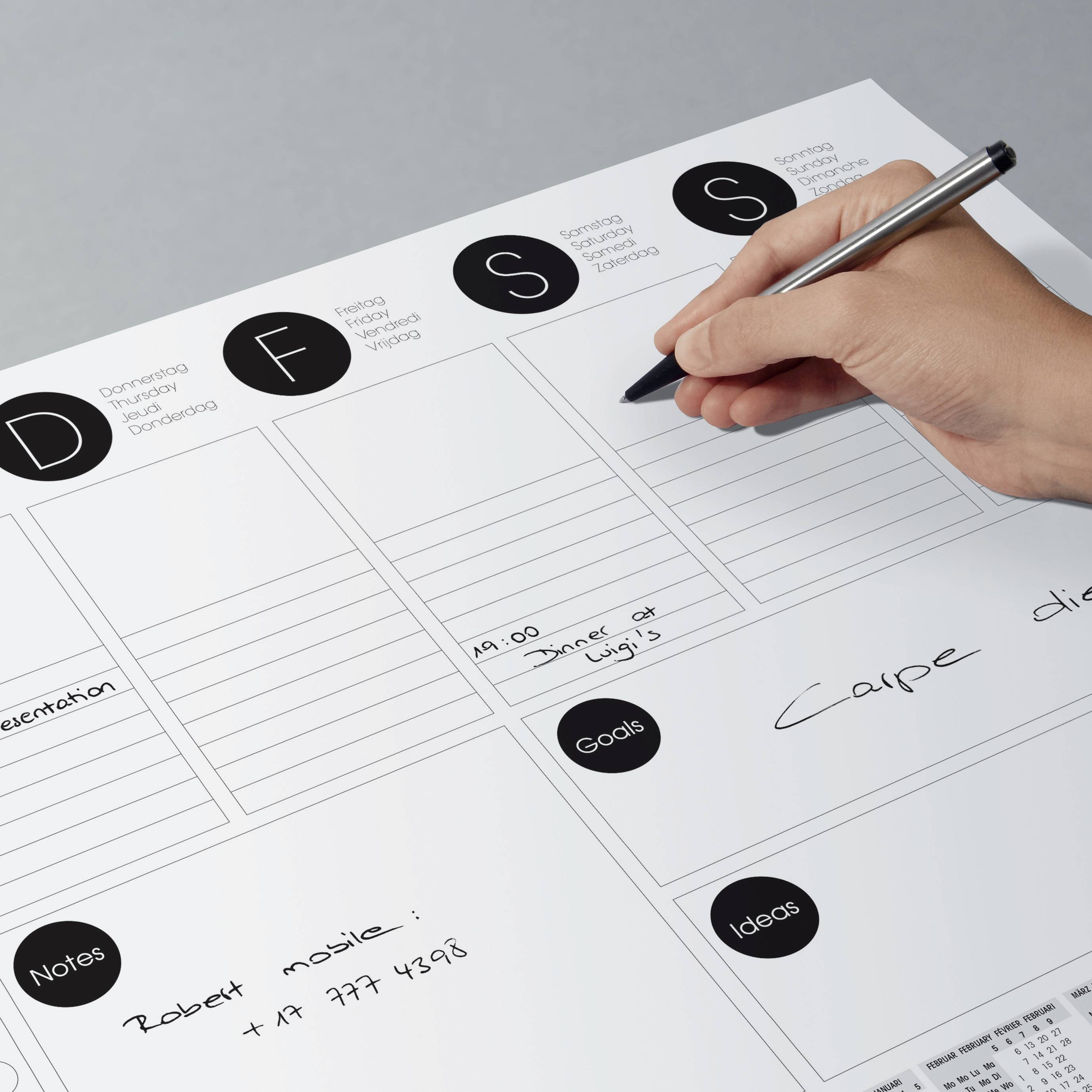 A hand is writing notes on a weekly planner. At the top are the days Monday through Sunday. Below are sections for tasks, goals, and ideas.