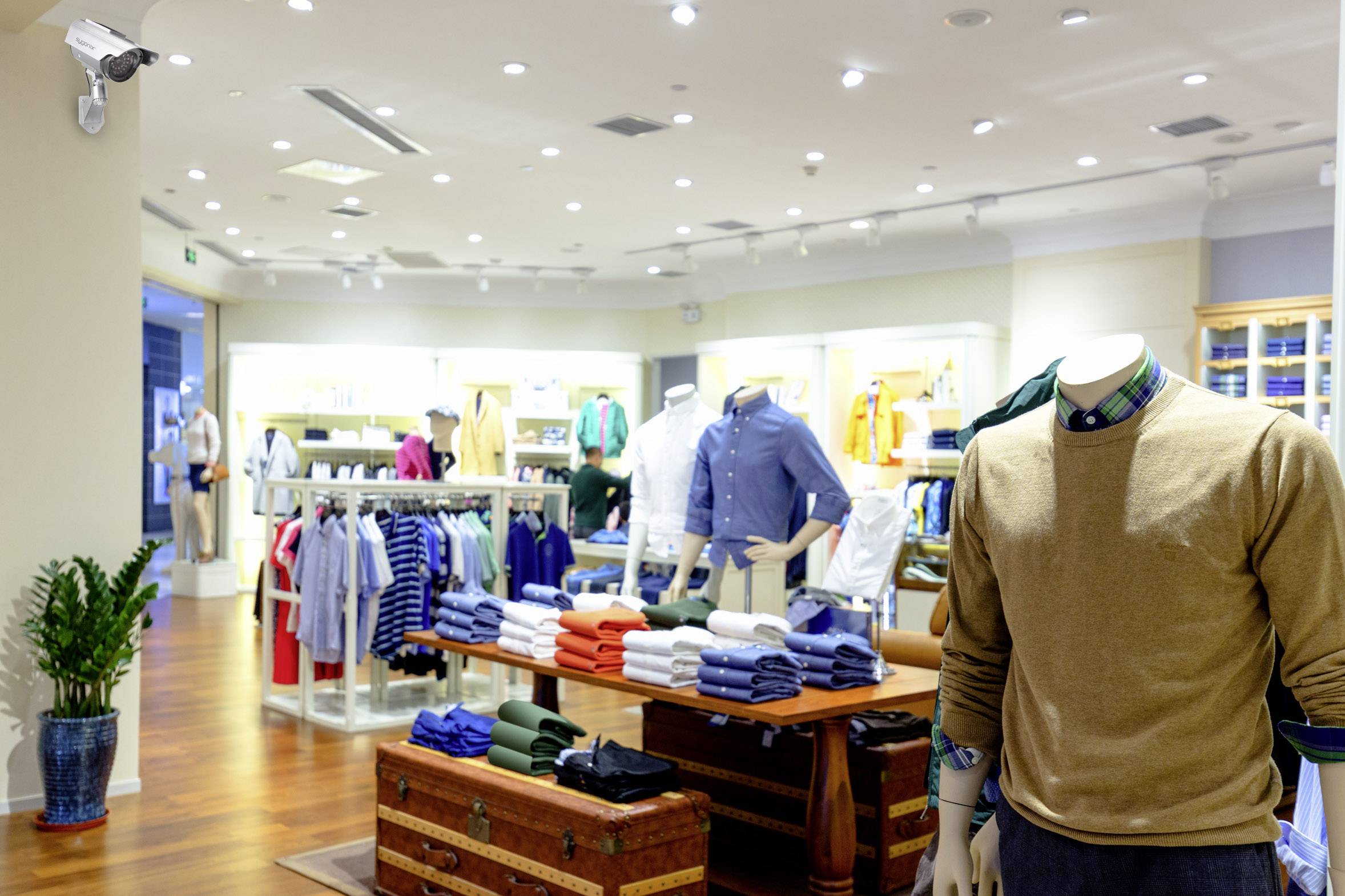 A modern clothing store with a wooden floor. On the left are clothing racks, and on the right, a suit is displayed on a mannequin torso.