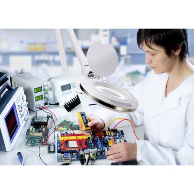 A person in a laboratory is working on electronic components on a circuit board, surrounded by measuring instruments and a magnifying glass.
