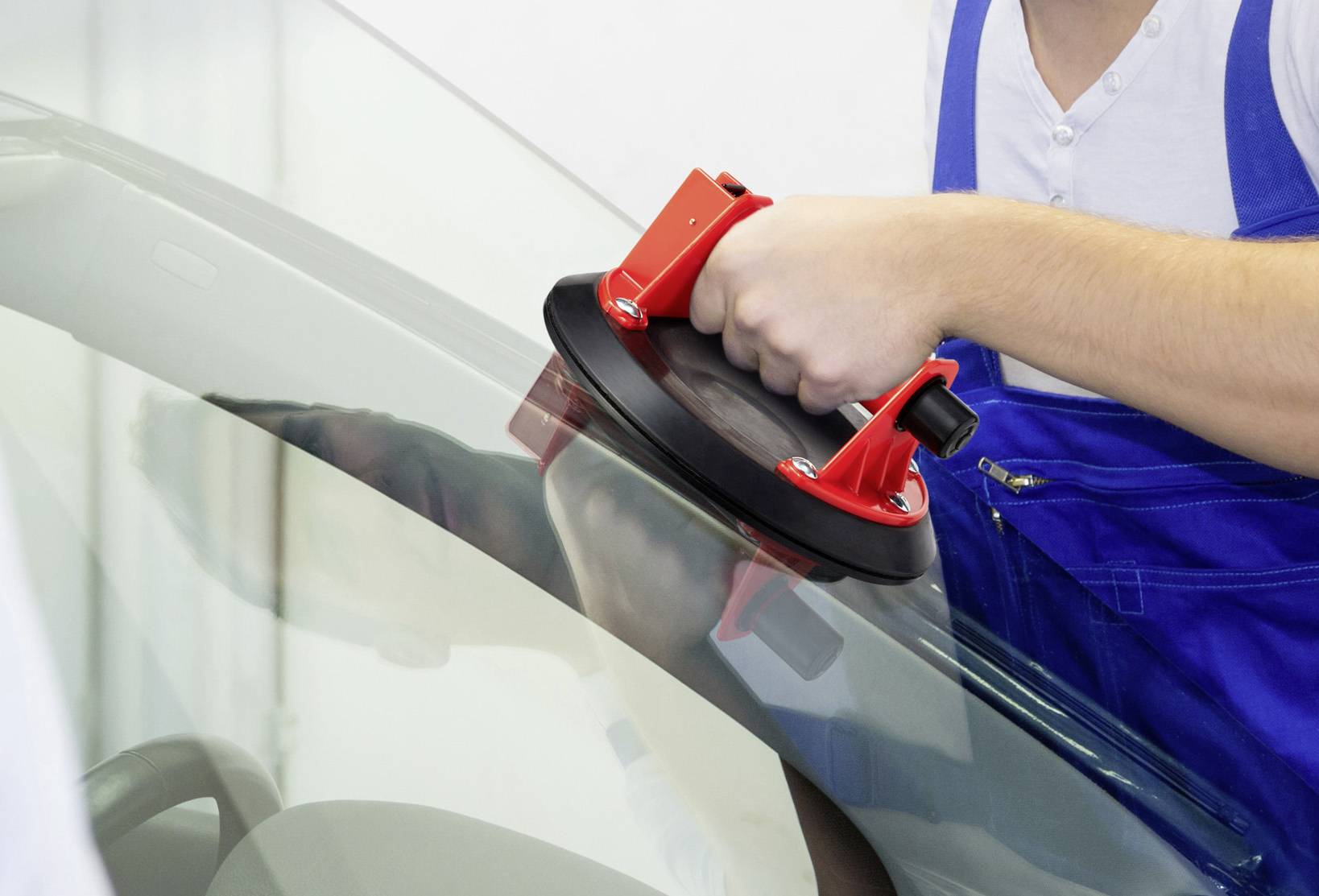 A person in blue workwear is using a suction cup to move a glass pane.