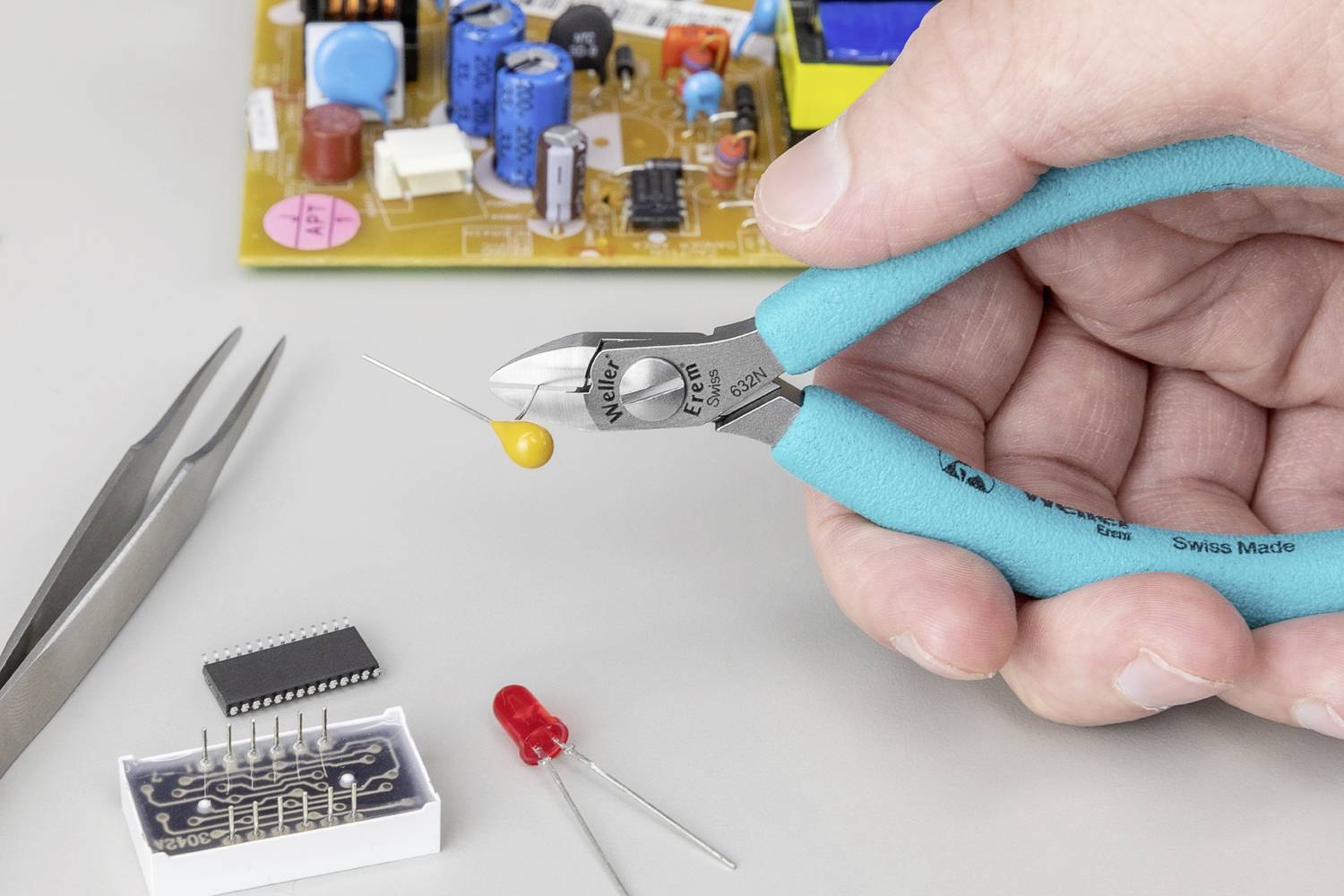 'Close-up of a hand using side cutters to cut an electronic component. A circuit board is visible in the background.'