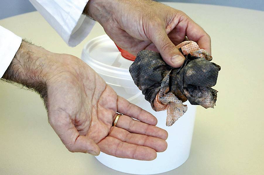 Two hands are holding a dirty, wet cloth over a bucket. The focus is on cleaning or waste management.