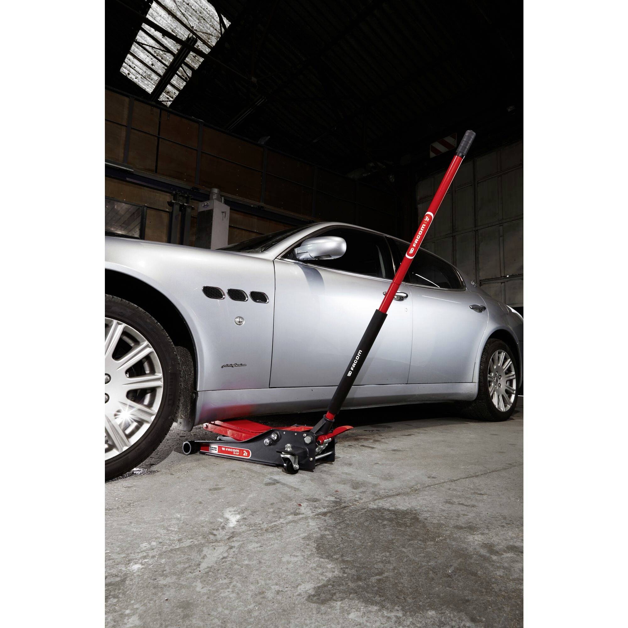 Silver car being raised on a red jack in a workshop. The focus is on the jack beneath the vehicle.