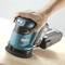 A hand is holding a blue Makita cordless sander, which is being moved over a smooth wooden surface.