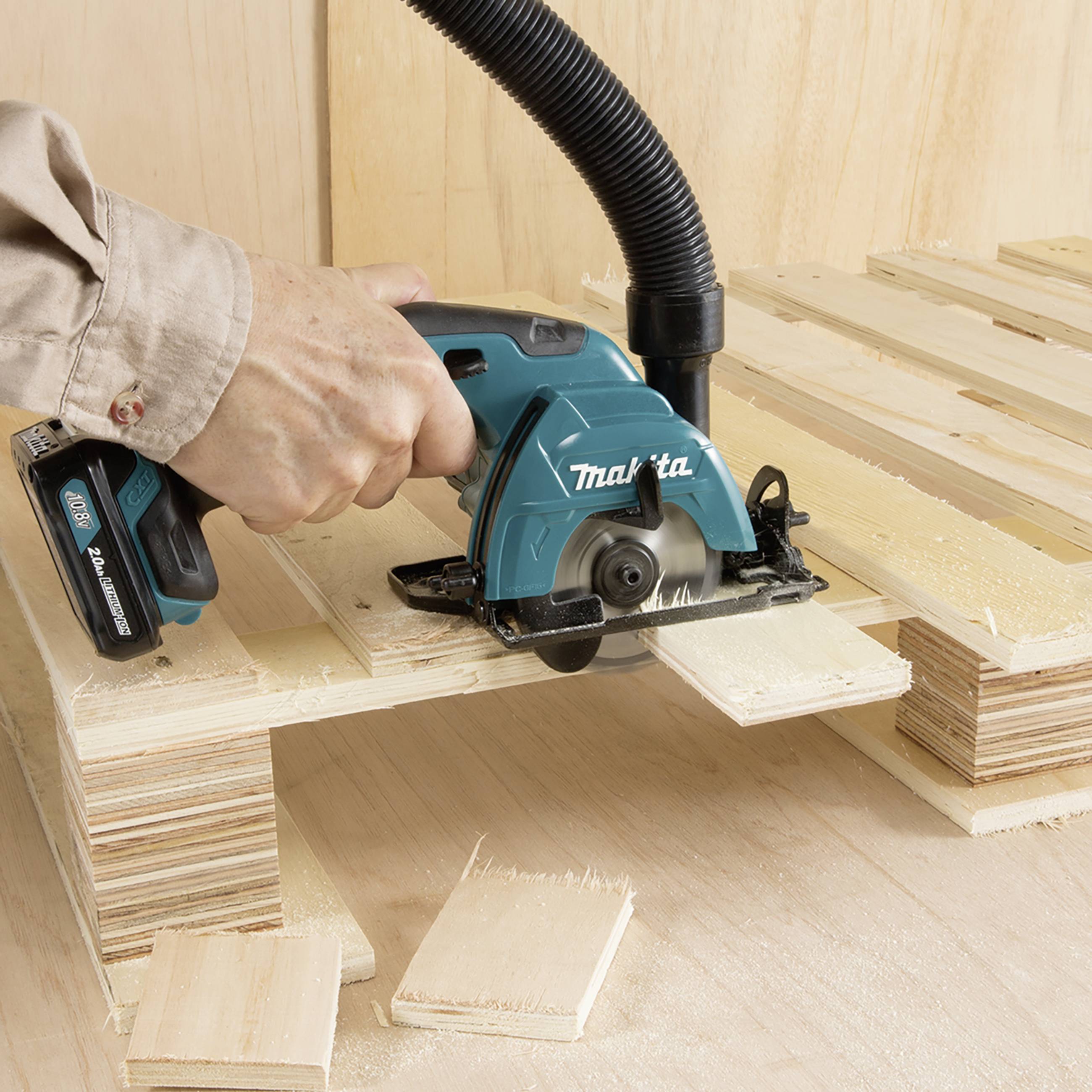 A worker is cutting wooden boards with a handheld circular saw. Sawdust flies as the machine processes the wood.
