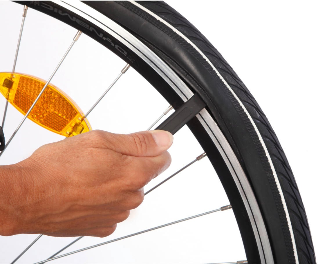 A hand is using a tyre lever to remove a bicycle tyre. The tyre lever is being positioned between the tyre and the rim.