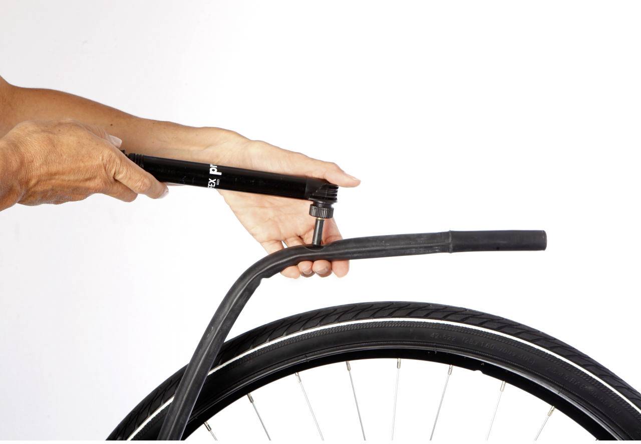 A person is inflating a bicycle tyre. They are holding a hand pump, which is attached to the valve of the tyre.