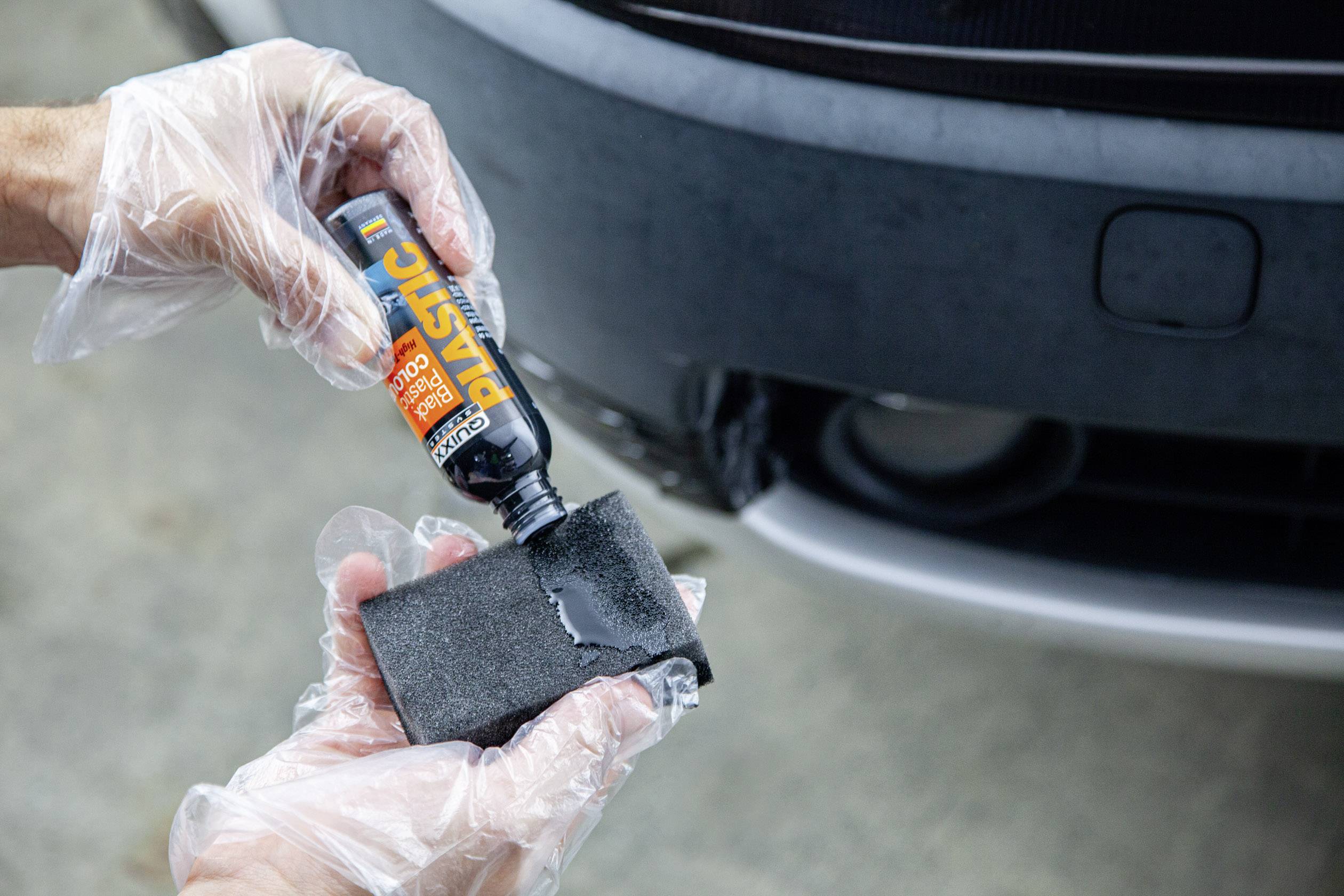 A person is applying a plastic restoration solution to a car bumper with a sponge to renew it.