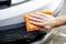 'A hand is cleaning the wet, soapy car at the bumper with an orange cloth.'