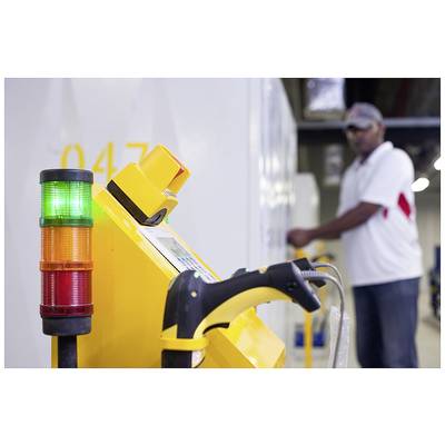 Yellow control device with a multi-coloured signal light in the foreground, man working blurrily at a control panel in the background.