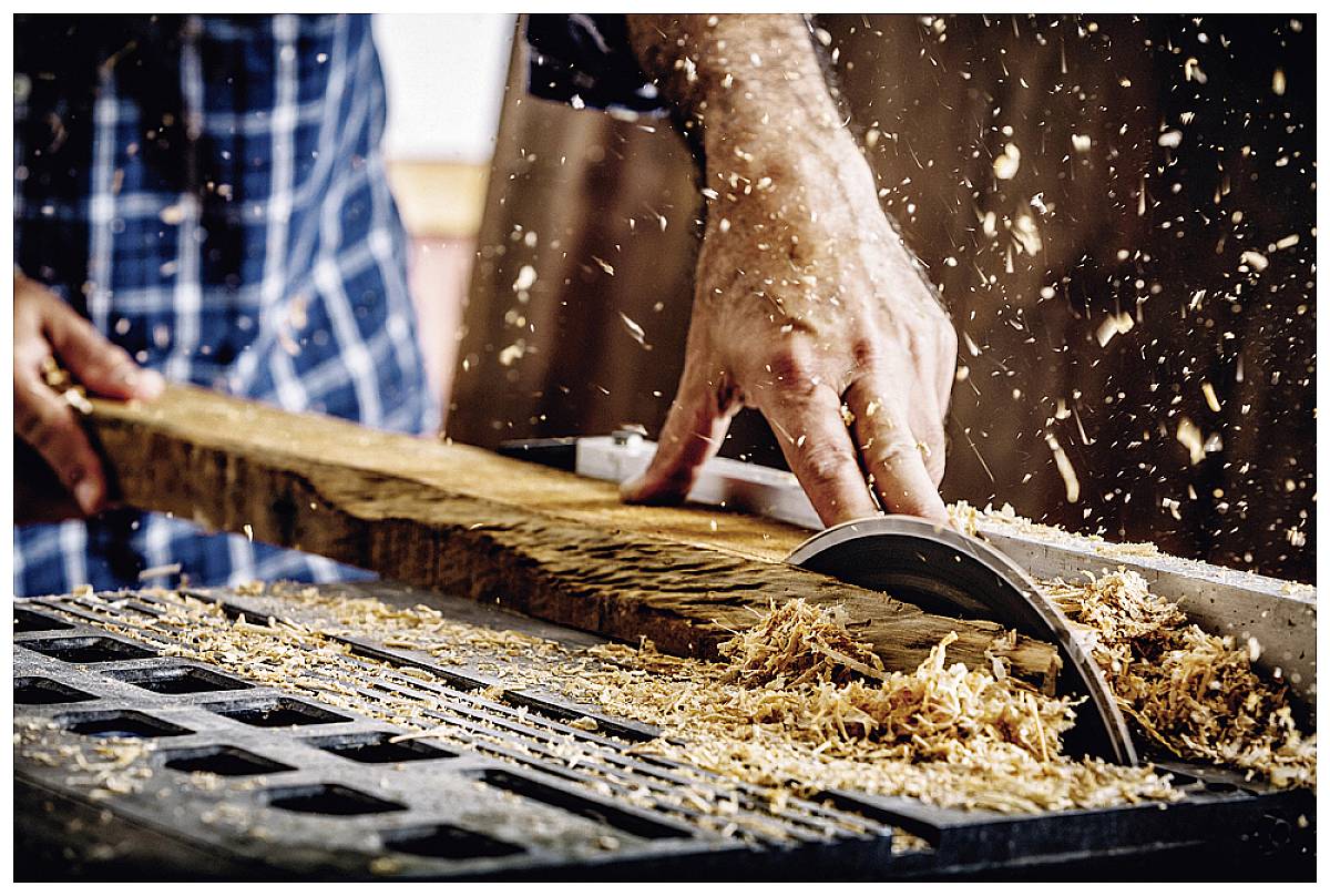 A person is cutting wood with a circular saw. Wood shavings are flying around. The scene depicts skilled craftwork in a workshop.