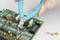 Someone is using side cutters to remove a wire from a printed circuit board. Resistors and capacitors are visible on the board.